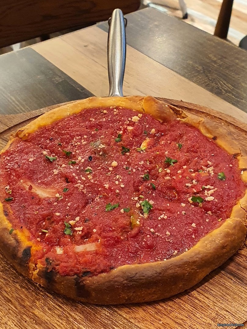 A deep-dish pizza with tomato sauce and herbs sits on a wooden board.