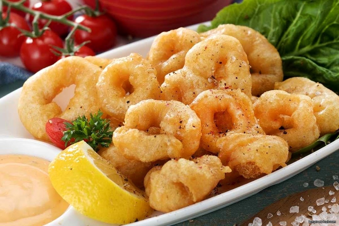 A plate of fried calamari rings with lemon, sauce, and tomatoes.