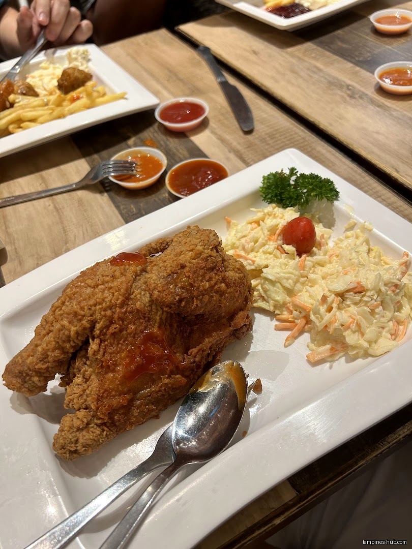 A plate of fried chicken with coleslaw and sauces on a wooden table.