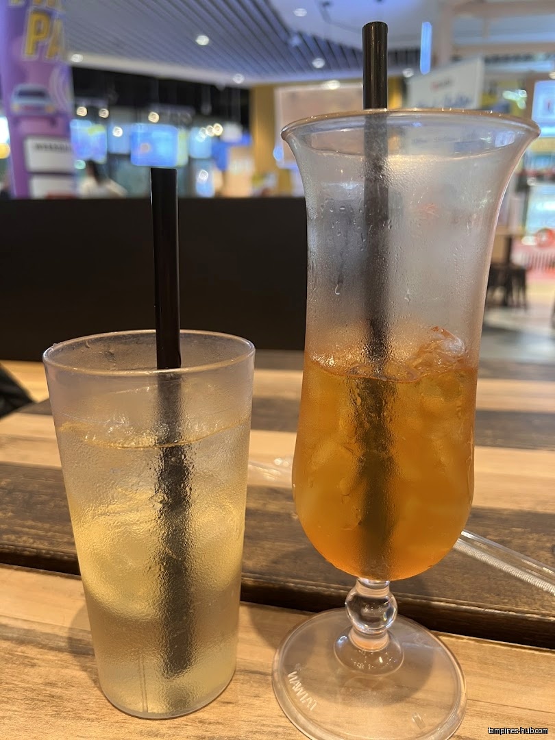 Two glasses of iced drinks with straws sit on a wooden table.