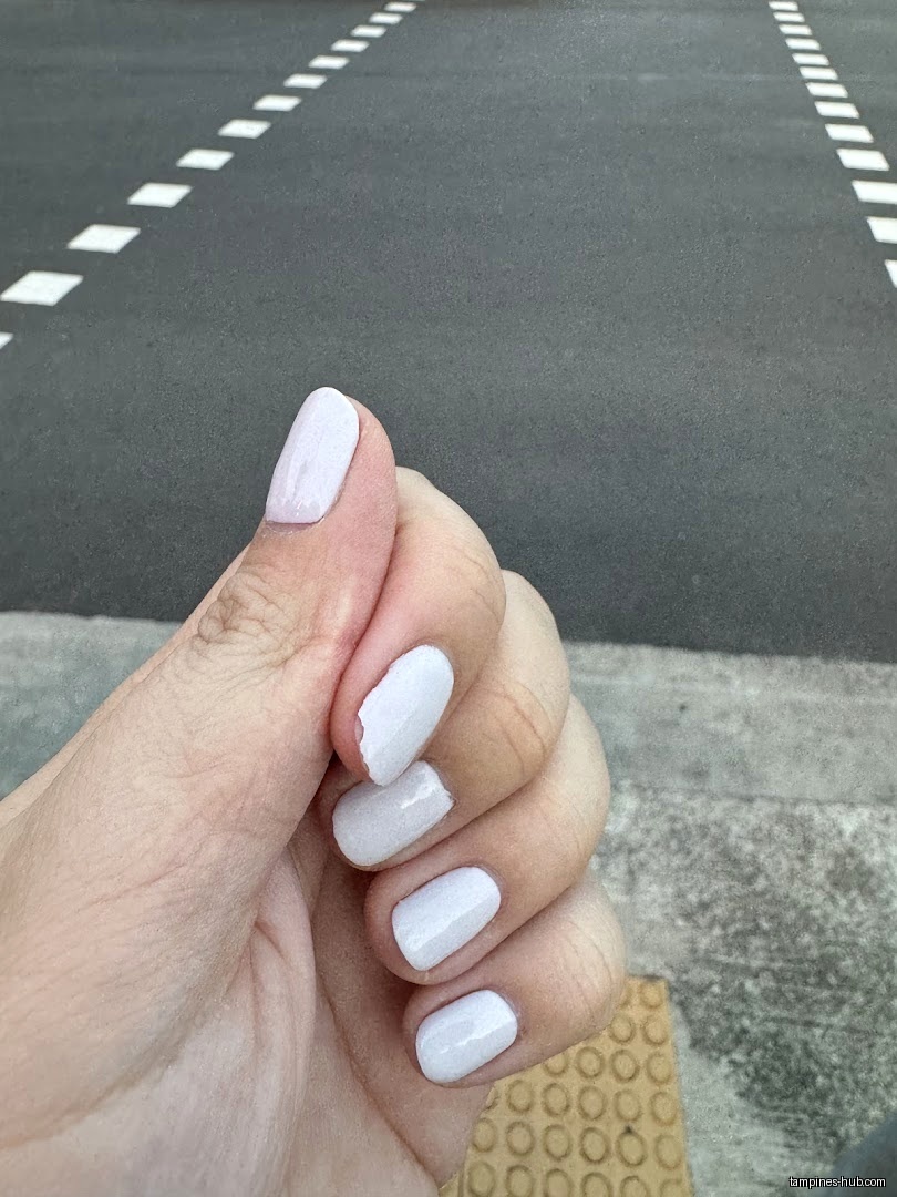 A hand with white nail polish is shown against an asphalt background.
