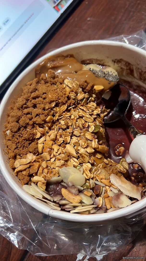 Açaí bowl with granola, nuts, seeds, and a spoon, next to a tablet.