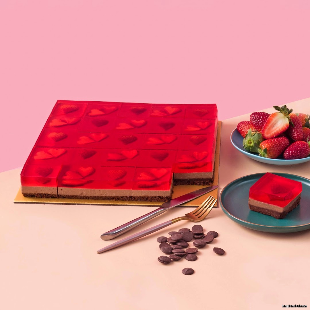 A red jelly cake with strawberries and chocolate chips on a table.