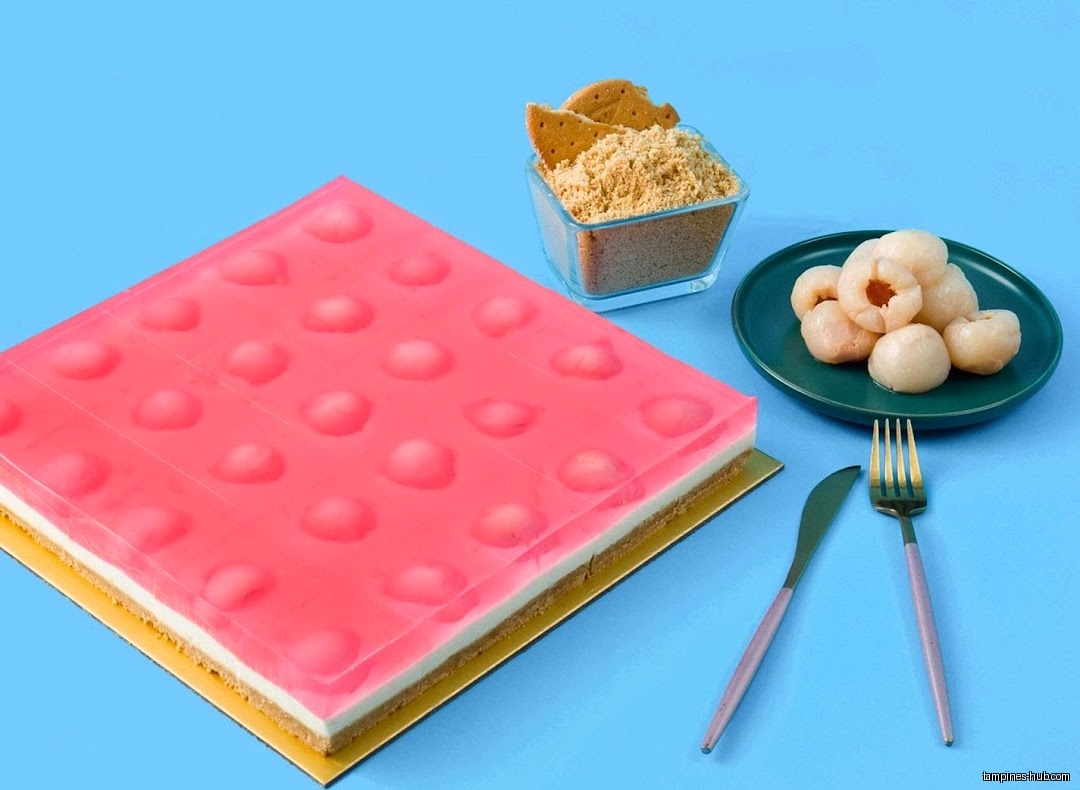 A pink jelly cake with lychees and graham cracker crumbs on blue background.