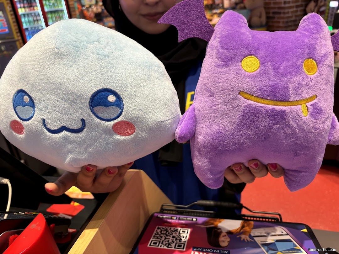 A person holds two plush toys: a blue cloud and a purple monster.