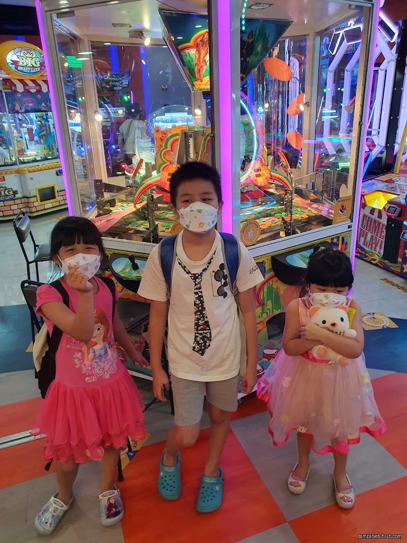 Three children wearing masks stand in front of arcade games at Timezone.