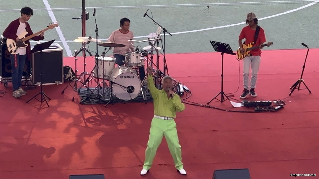 A band performs on a stage with a singer in a green suit.