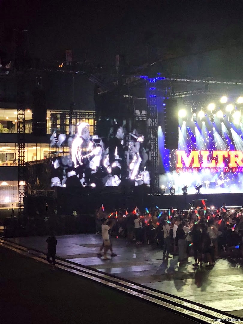 A crowd watches a concert with a large screen and stage lights.