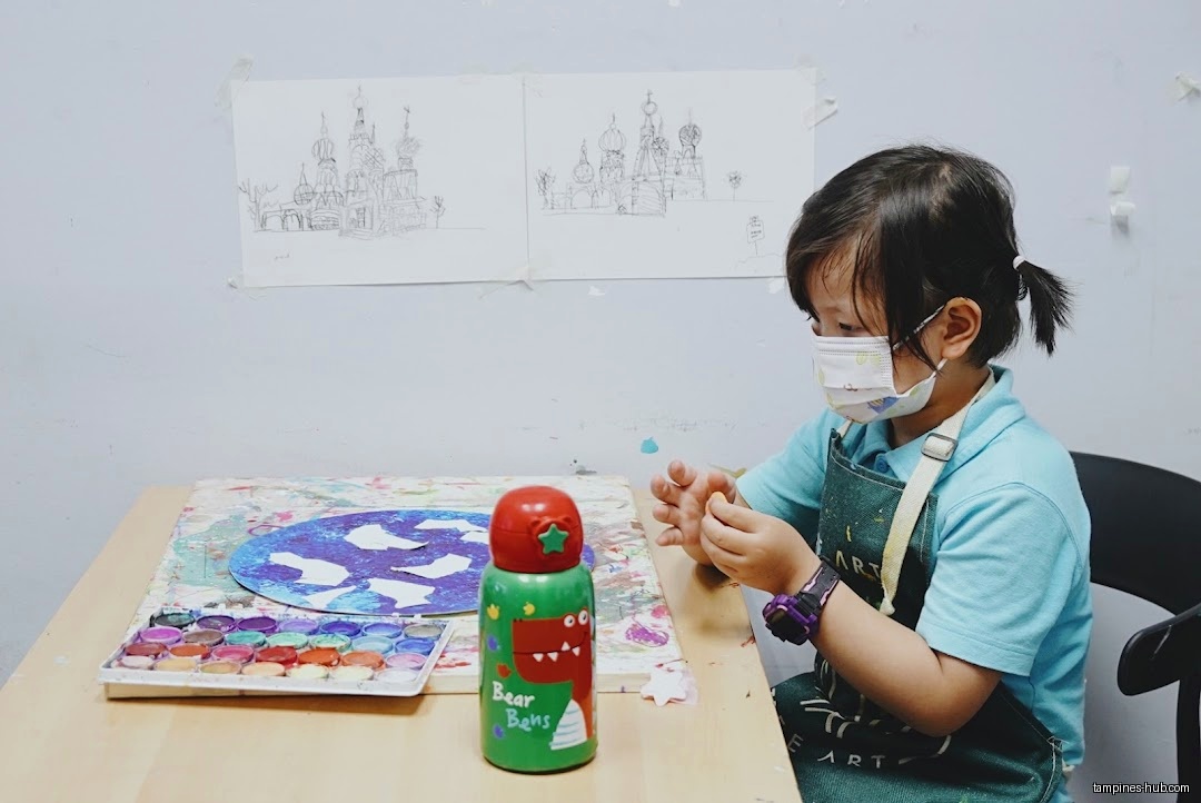 A child wearing a mask and apron works on an art project.
