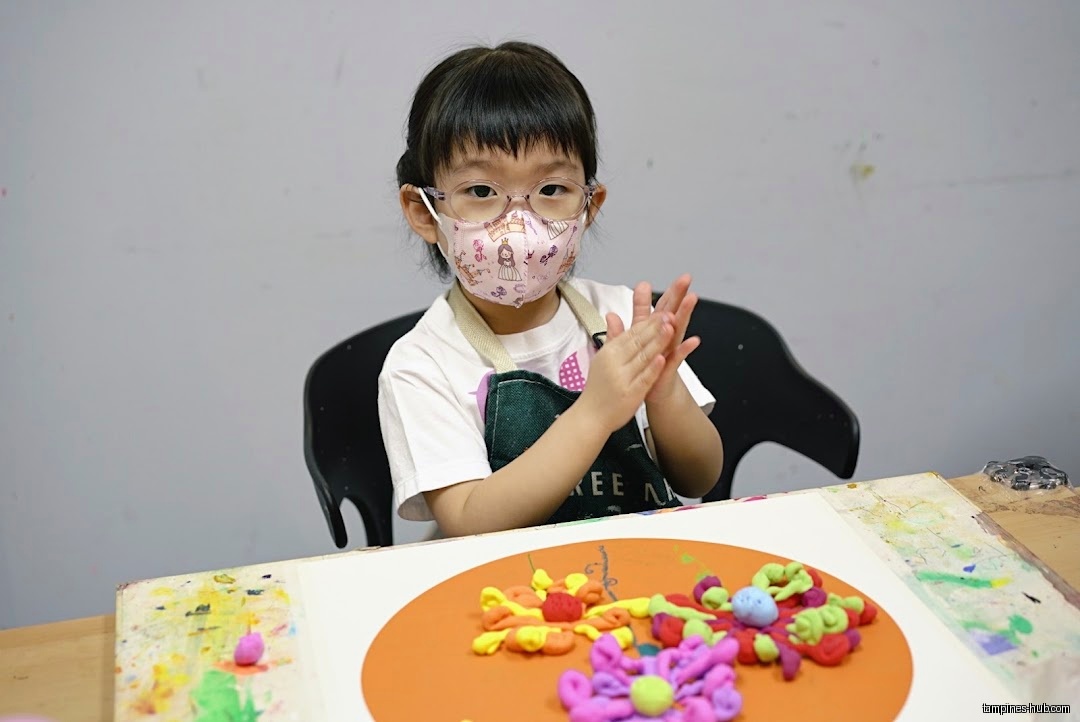 A young girl wearing a mask is doing clay art at a table.