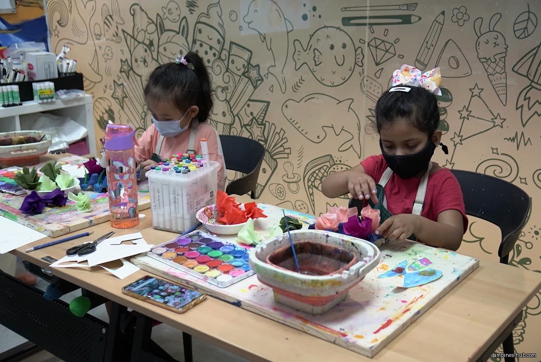 Two young girls wearing masks are crafting at a table with art supplies.