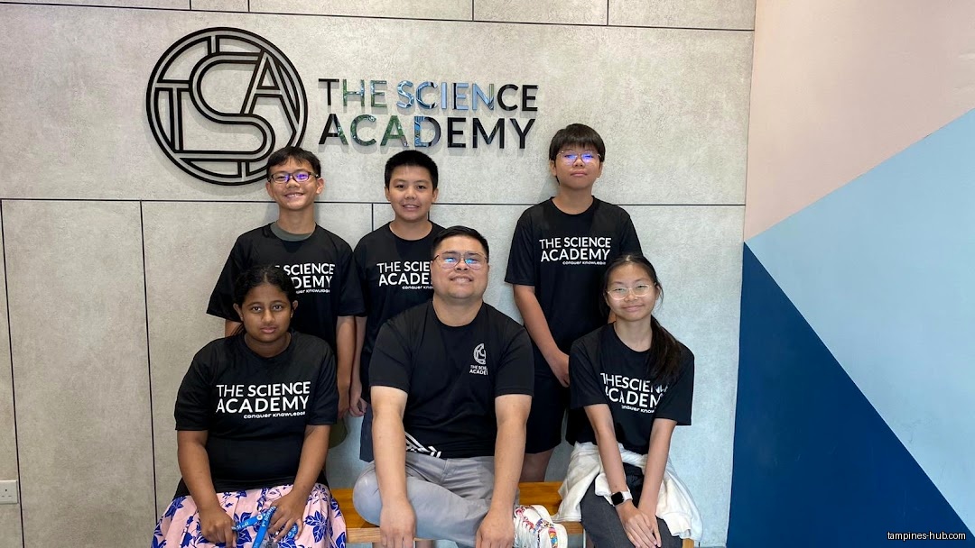 A group of students and a teacher pose in front of TSA's logo.