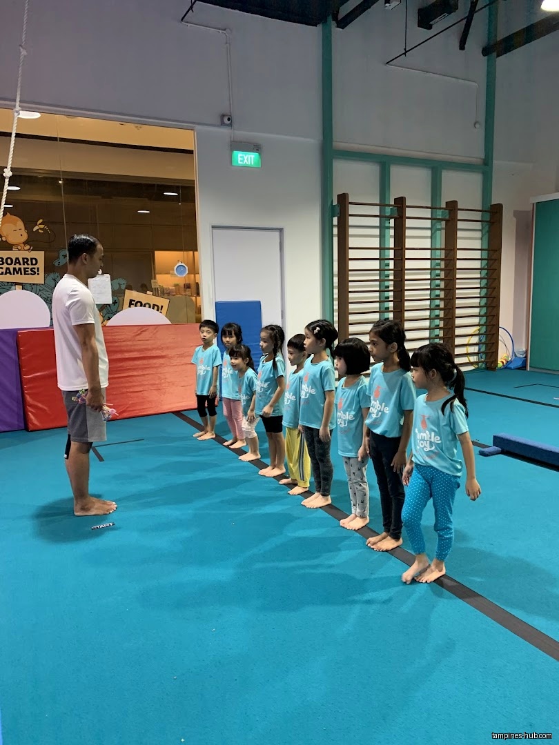 A gymnastics instructor leads a line of children in matching shirts.