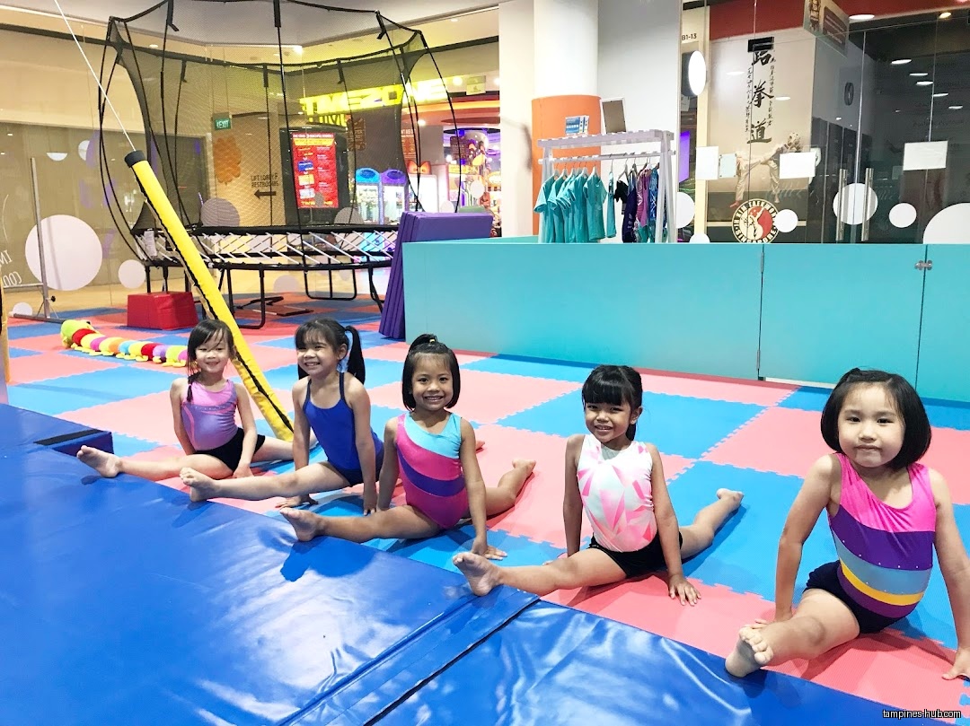Five young girls in leotards are doing splits in a gymnastics studio.