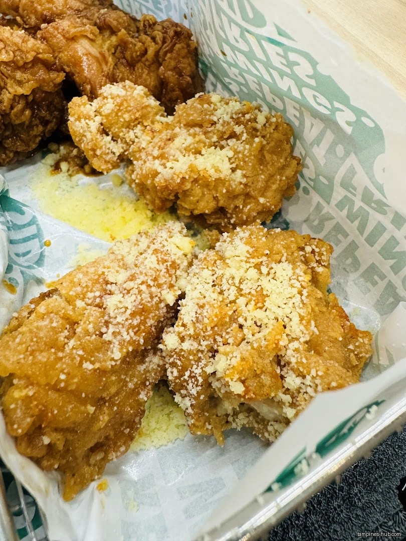 A close-up of fried chicken wings with grated cheese in a container.