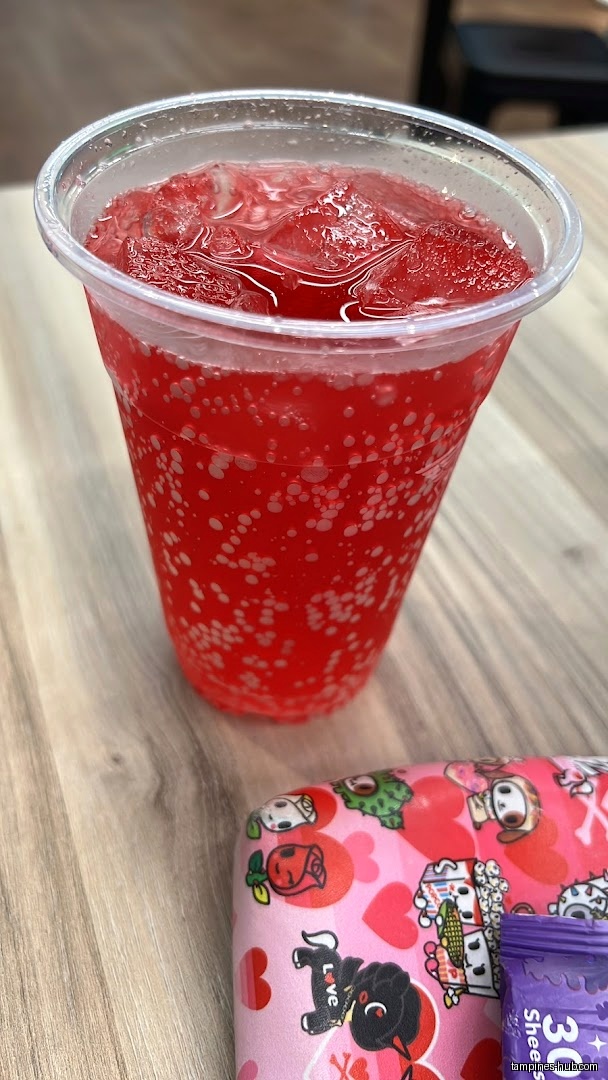 A red drink with ice and a pink case on a table.