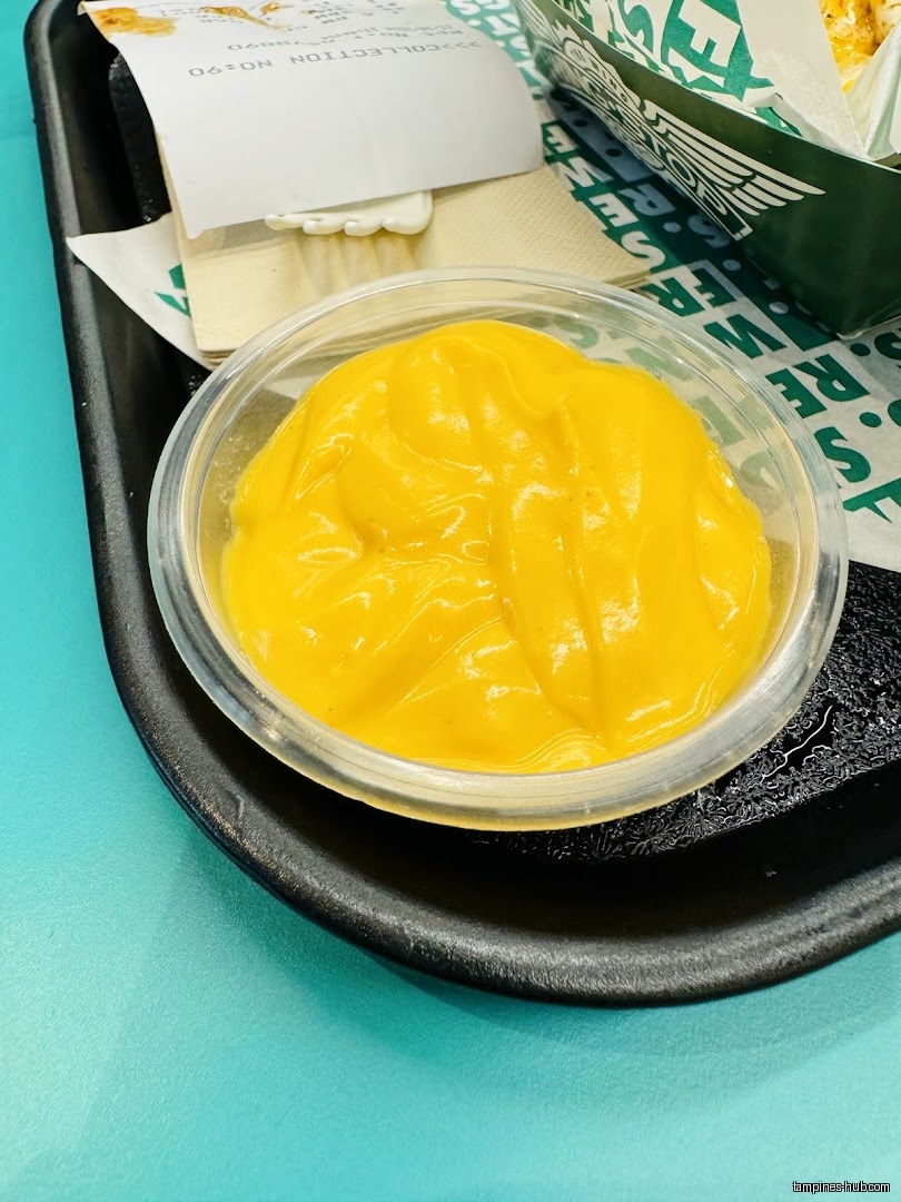 A small container of yellow sauce sits on a black tray.