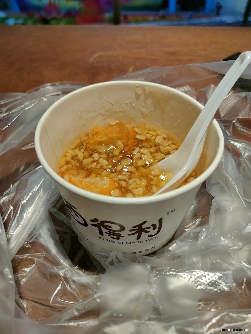 A cup of Xi De Li dessert with a spoon, in a plastic bag.