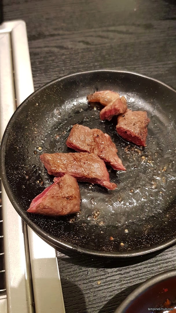 A black plate holds pieces of cooked meat, likely from Yakiniku Shokudo.