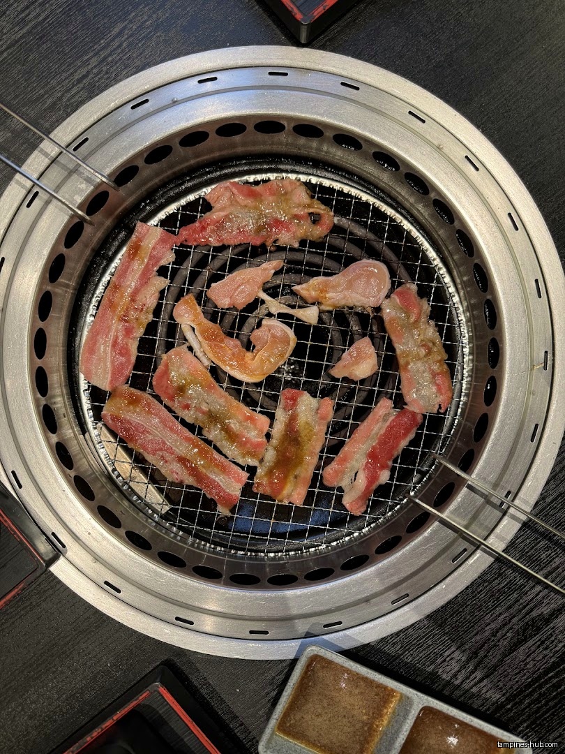 Thinly sliced meat is cooking on a grill at Yakiniku Shokudo.