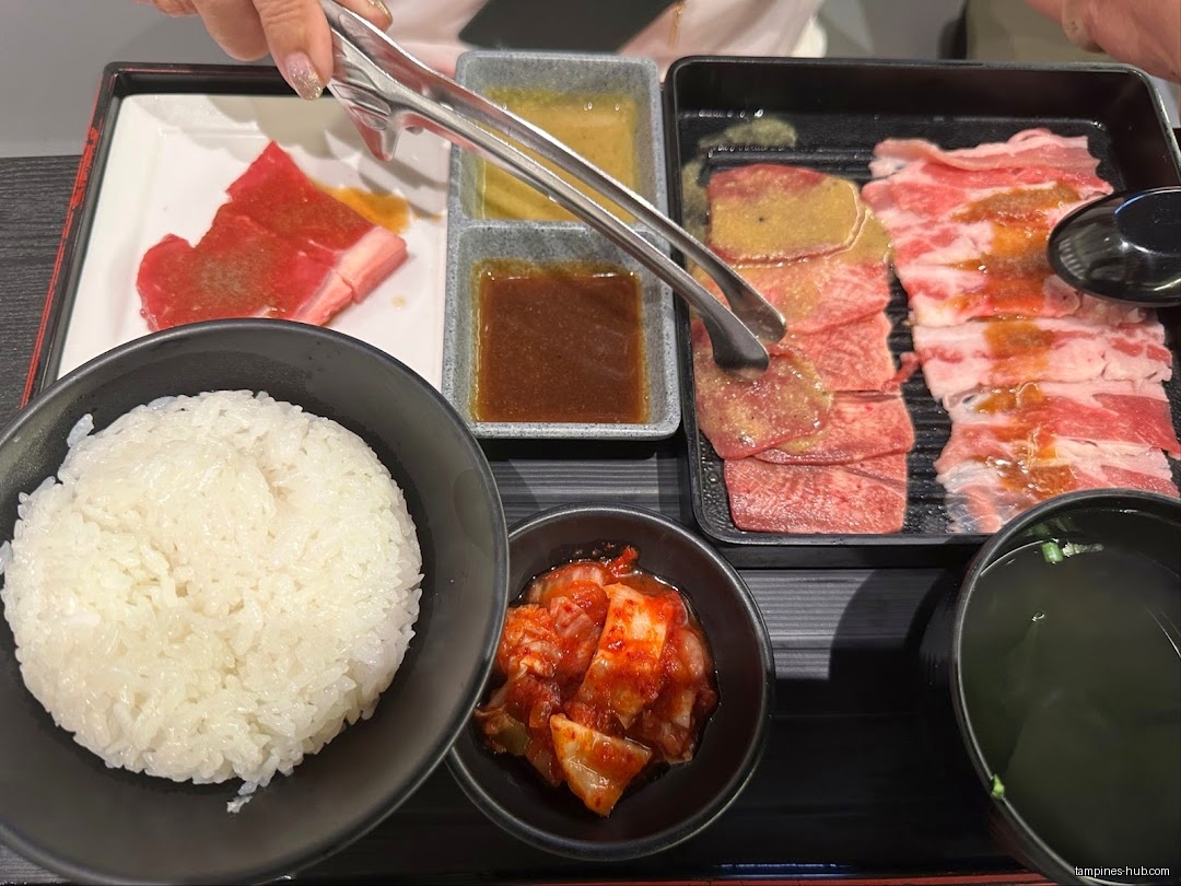 A yakiniku set meal with meat, rice, kimchi, soup, and dipping sauces.