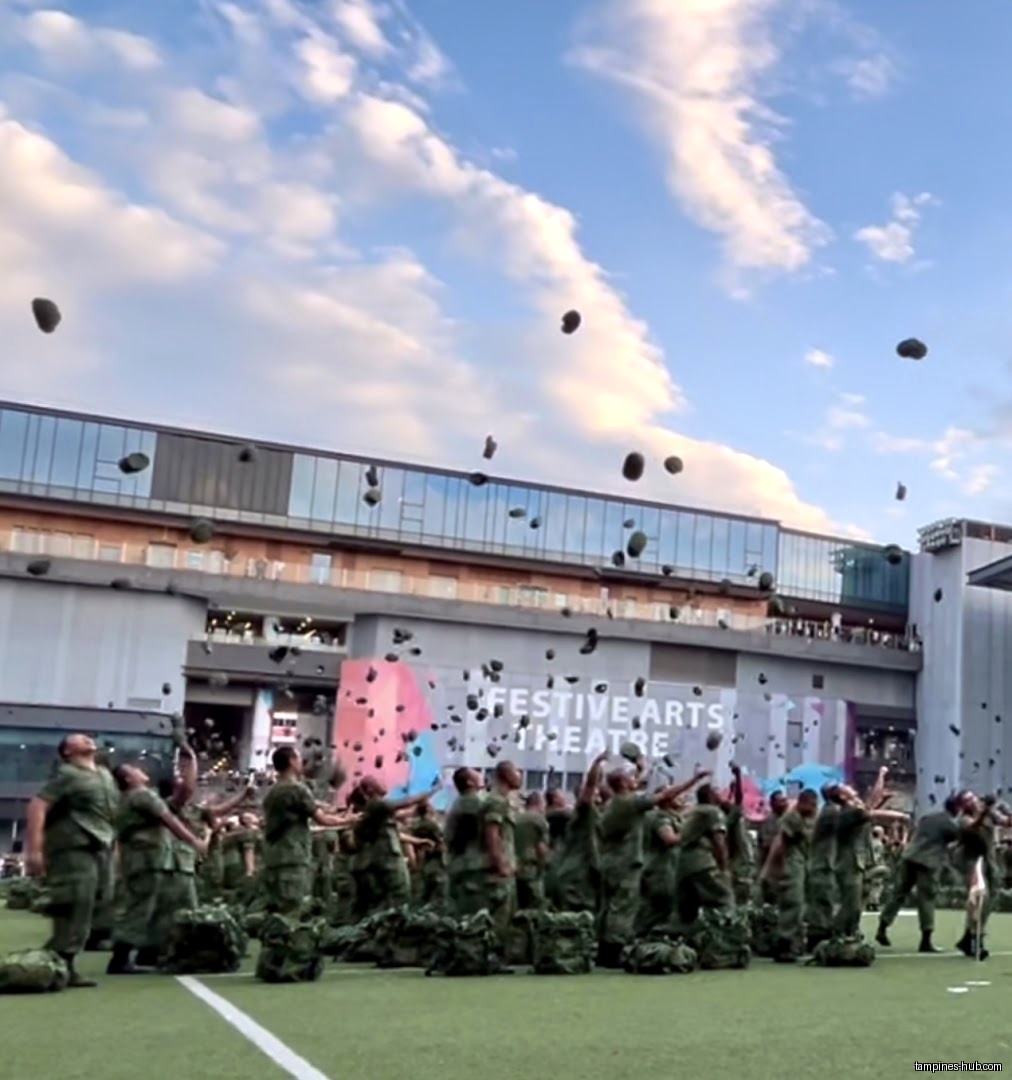 People in uniform throw hats in the air in front of a building.