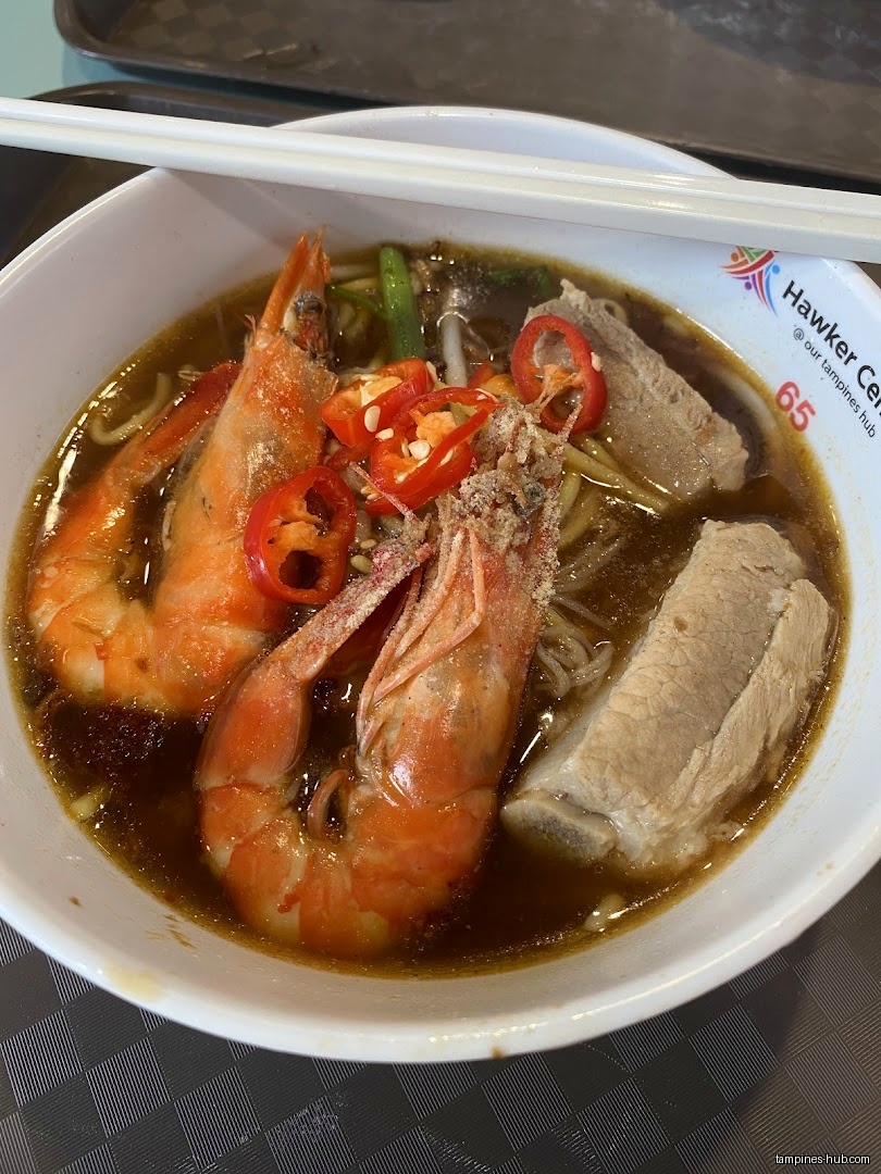 A bowl of prawn noodle soup with prawns, pork ribs, and chili.