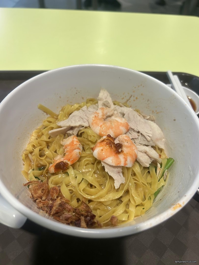 A bowl of prawn noodles with sliced meat and fried shallots.