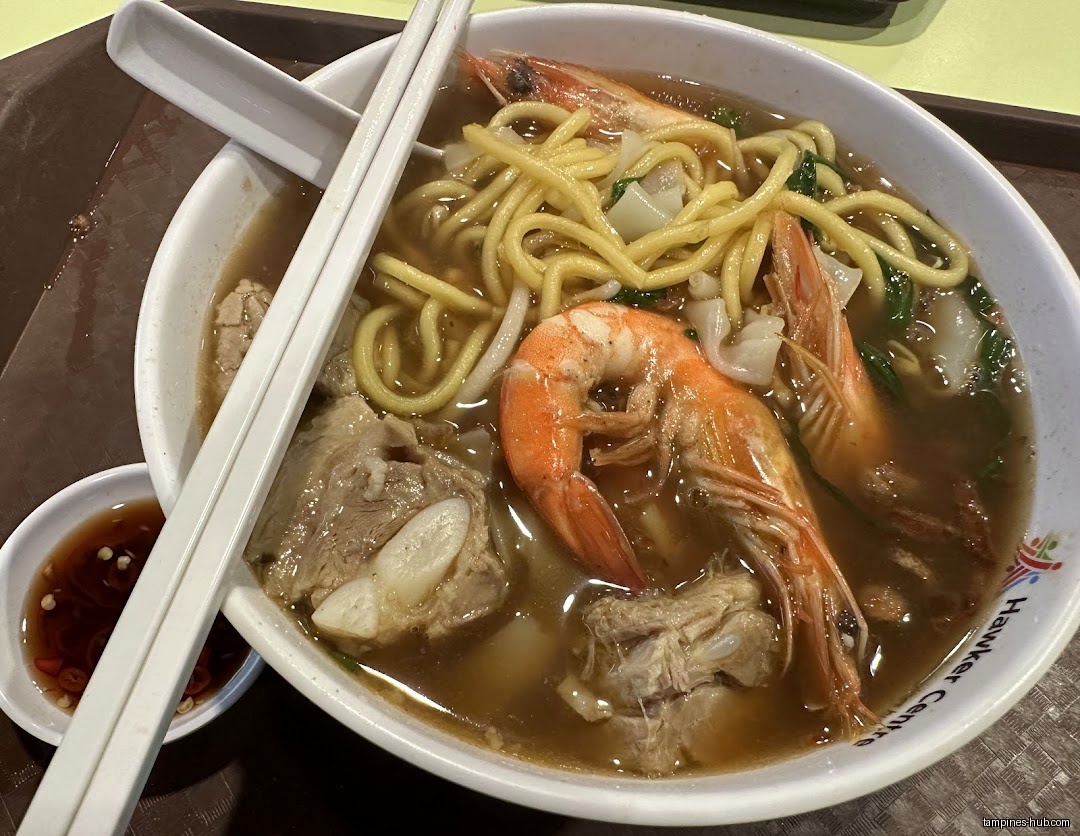 A bowl of prawn noodles with prawns, meat, and broth is shown.