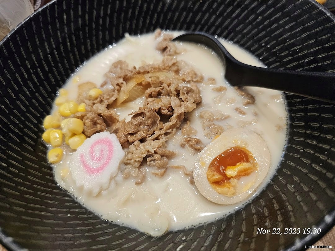 A bowl of ramen with beef, corn, egg, and fish cake.