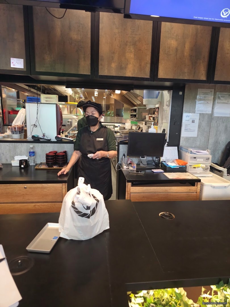 Yoshinoya staff member stands behind counter with a customer's bagged order.